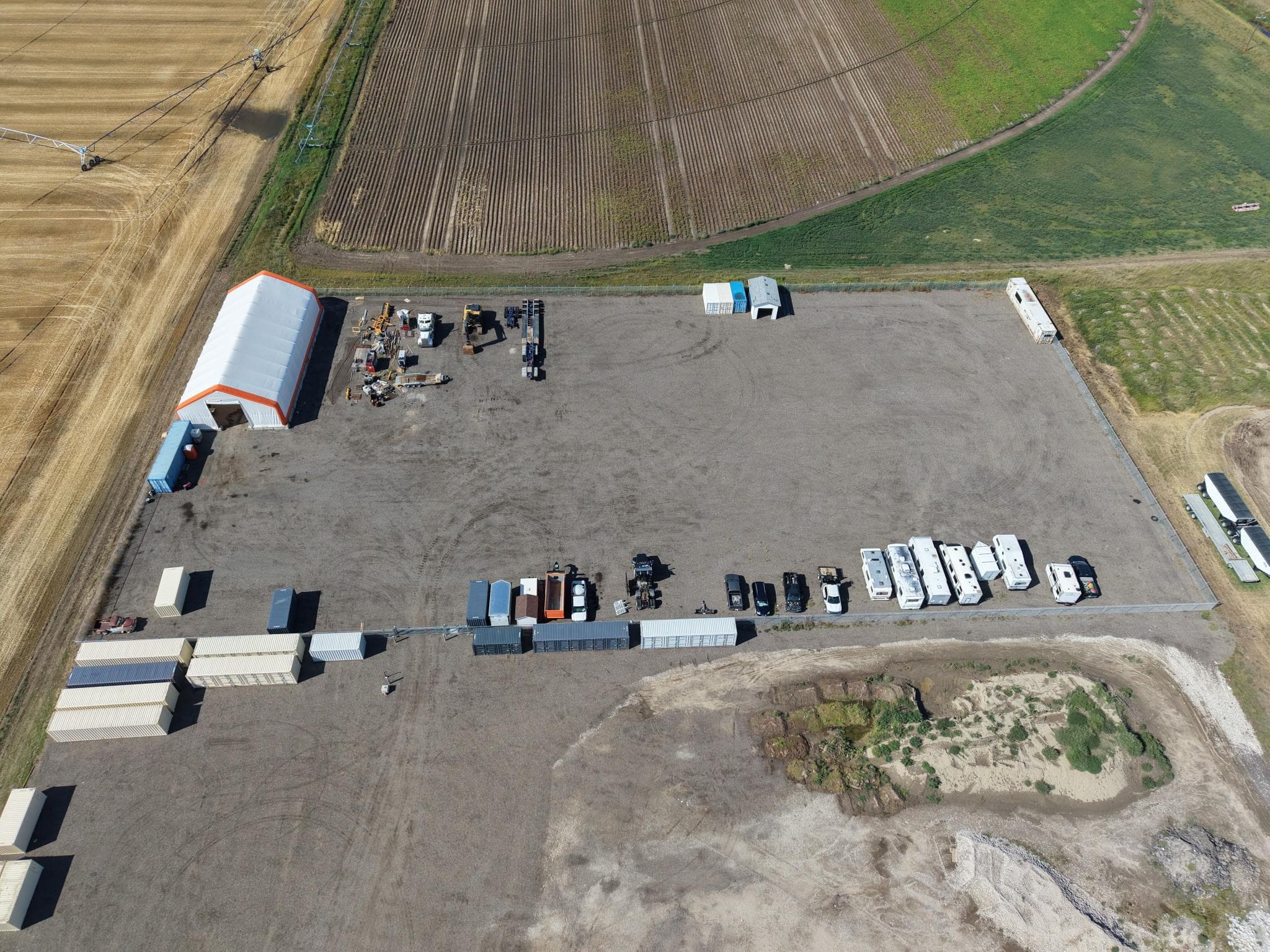 Bird’s-eye view of the gravel storage property, parked trailers, and surrounding farmland