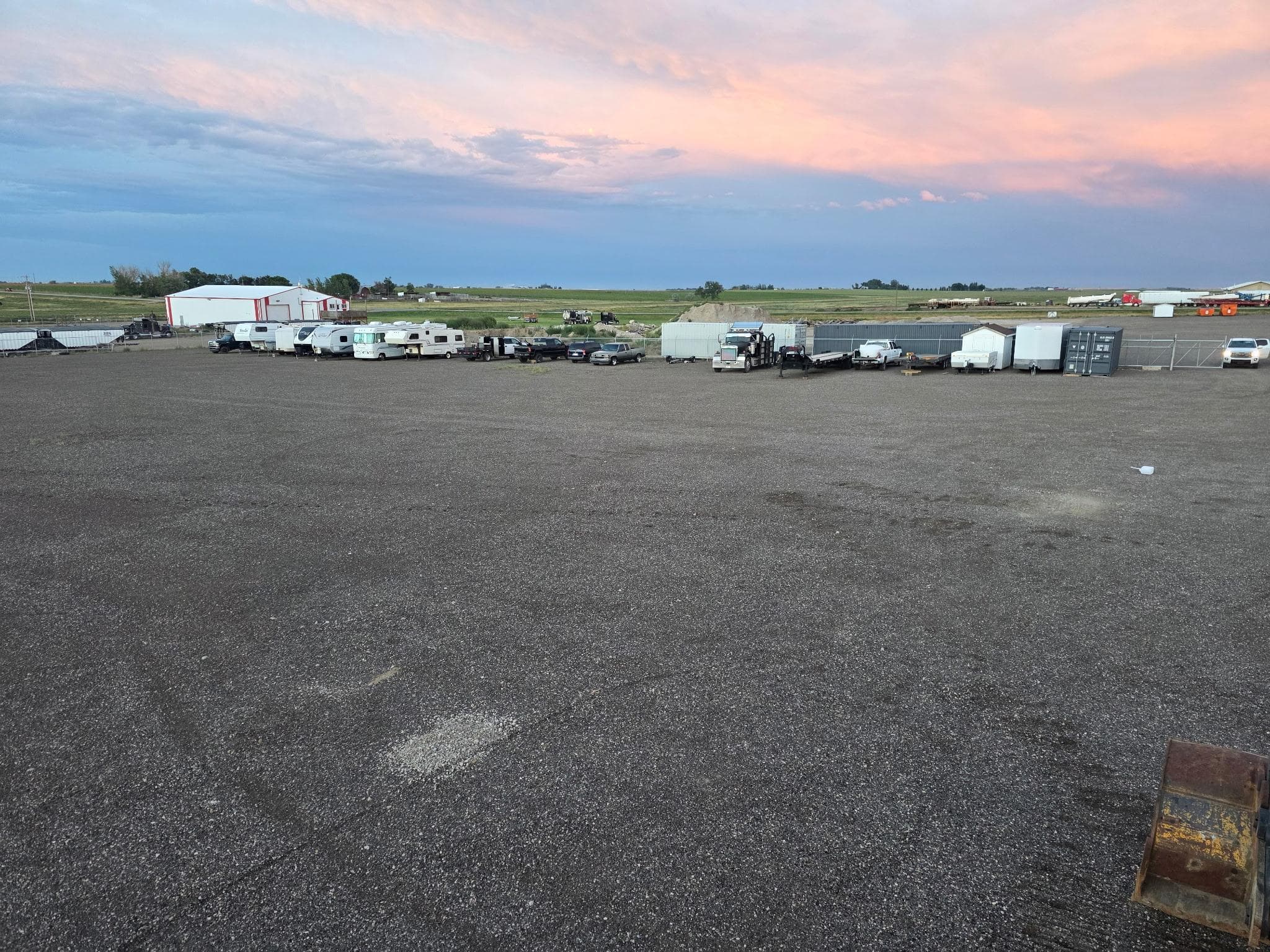 RVs and trailers parked on the gravel lot beneath a colourful evening sky